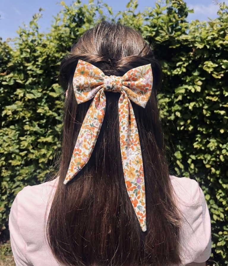 Pince nœud fleurie orange portée dans les cheveux